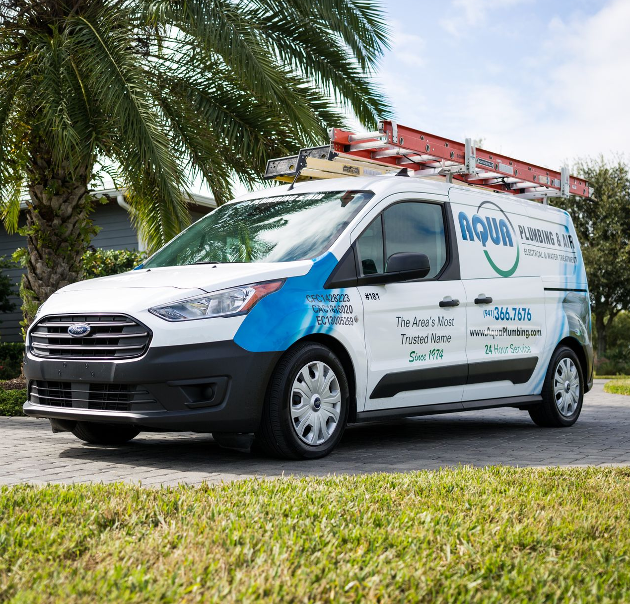 White Aqua plumbing van parked on a driveway with a ladder on top. Palm tree in background.