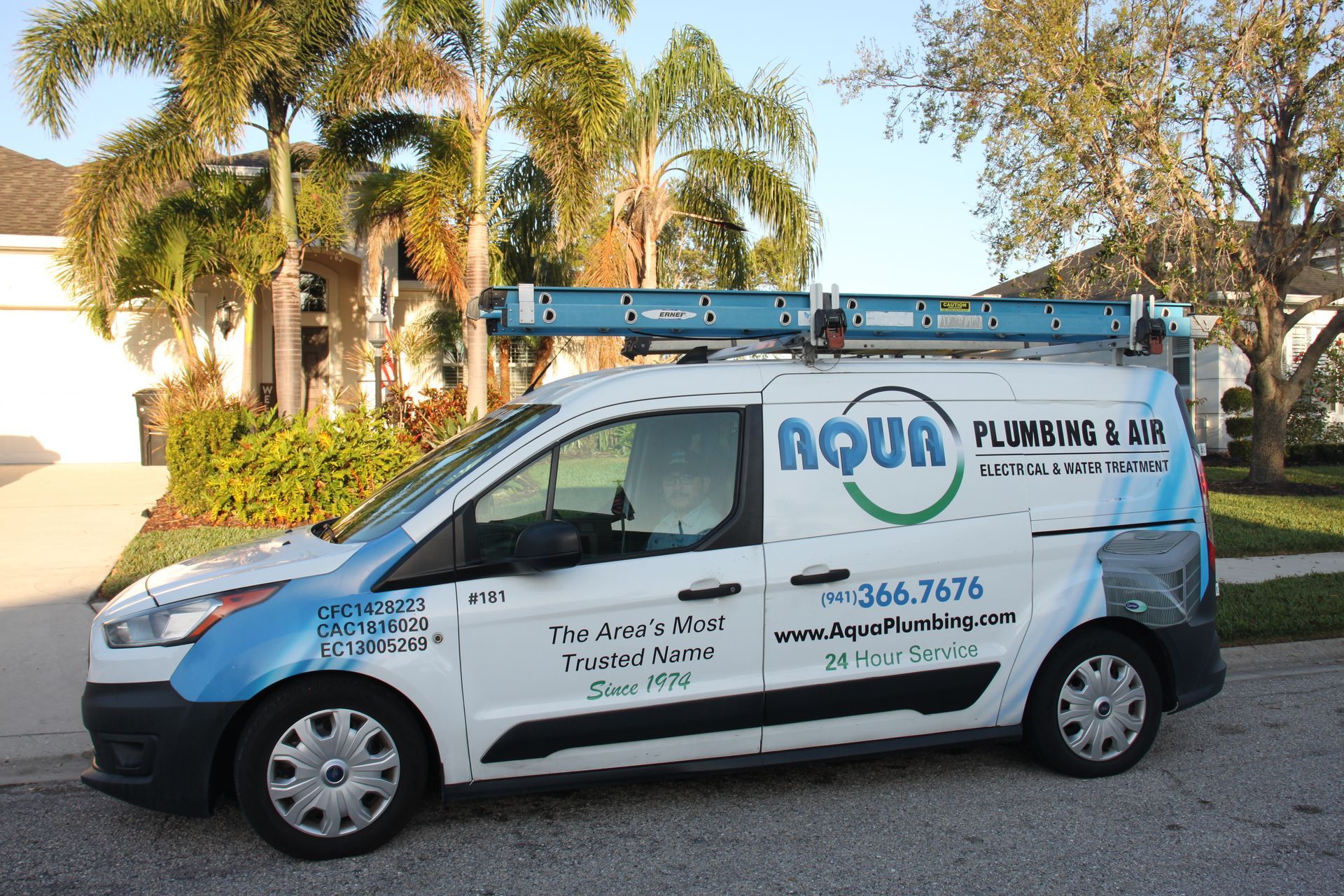 White van with Aqua Plumbing & Bids logo parked in front of a house, ladder on roof.
