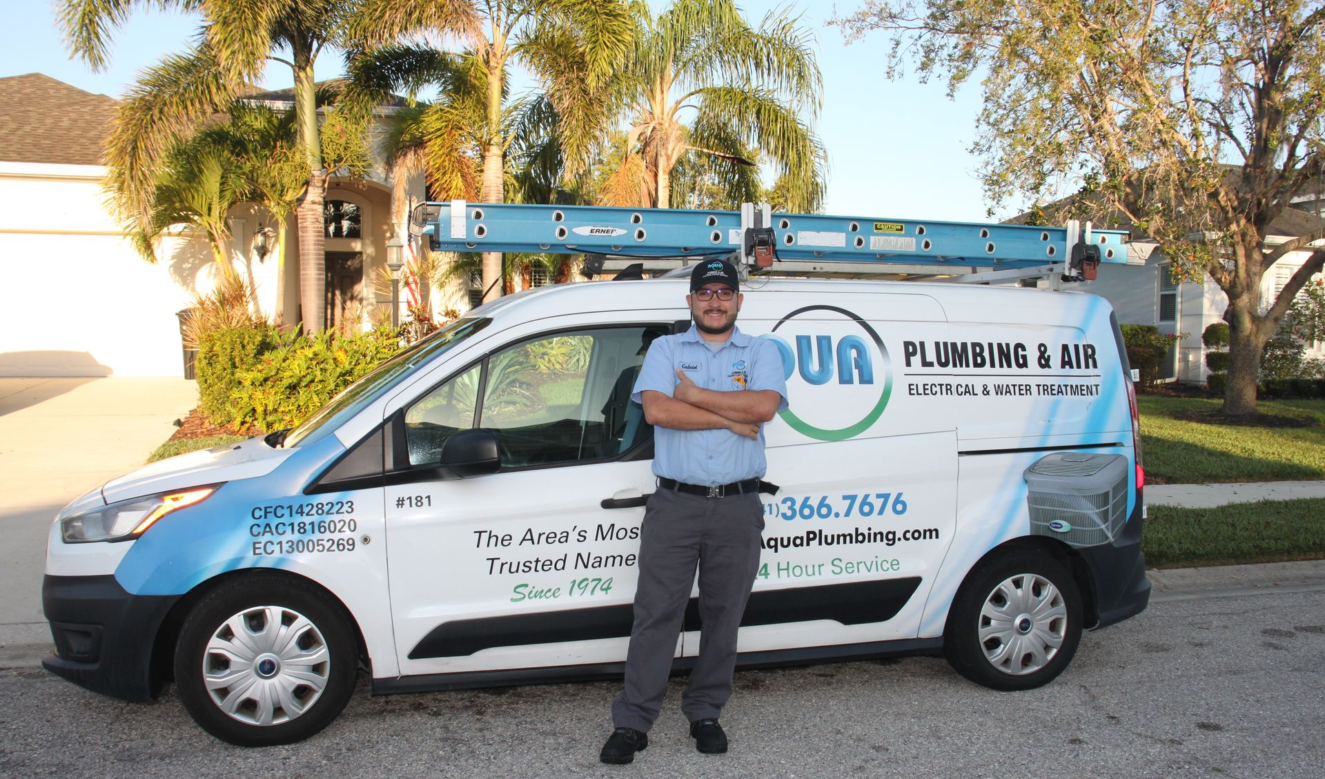 Plumber standing next to a van with tools on top. The van has the company logo and phone number printed on the side.