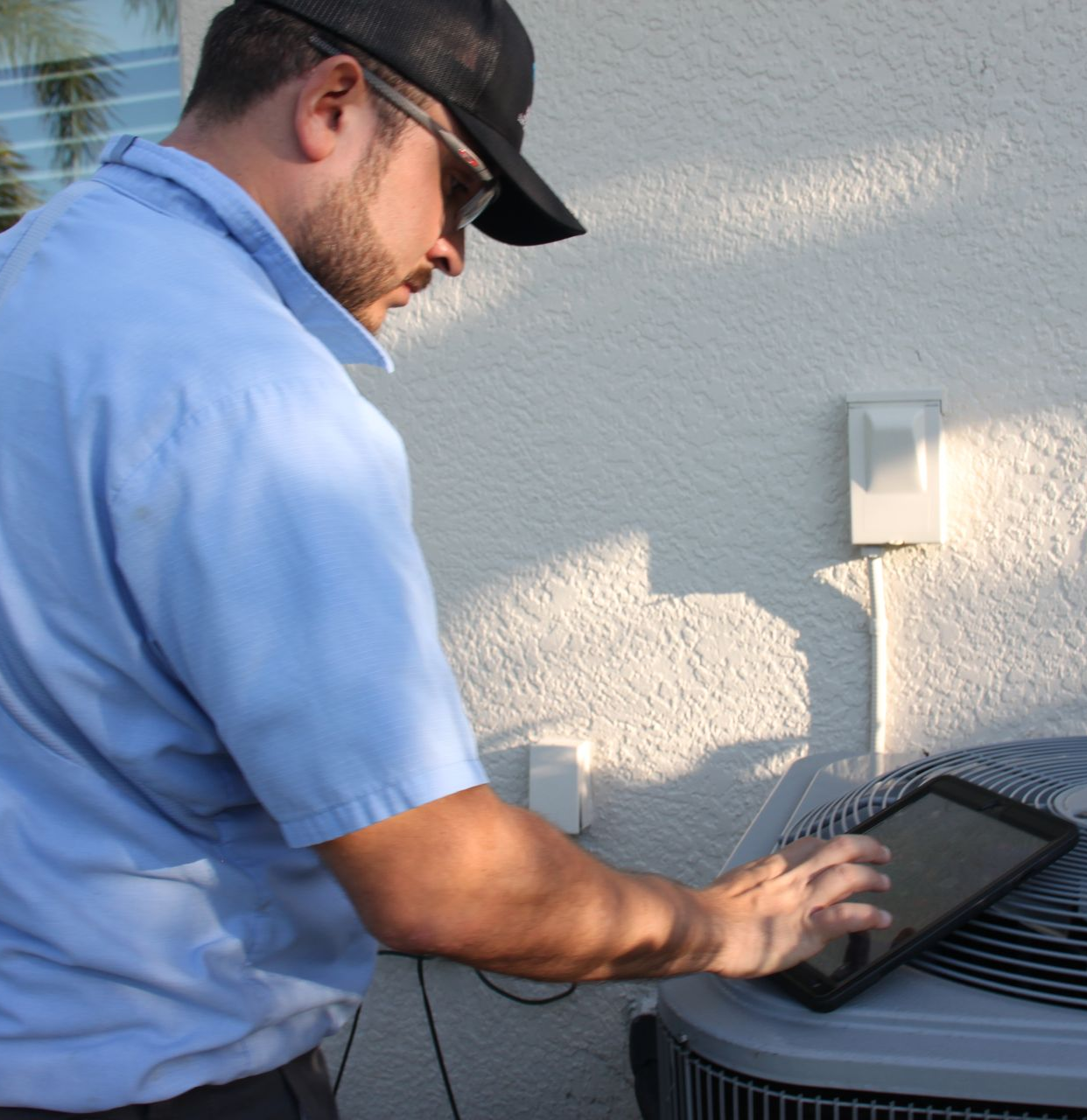 HVAC technician using a tablet, inspecting an air conditioning unit outside a building.