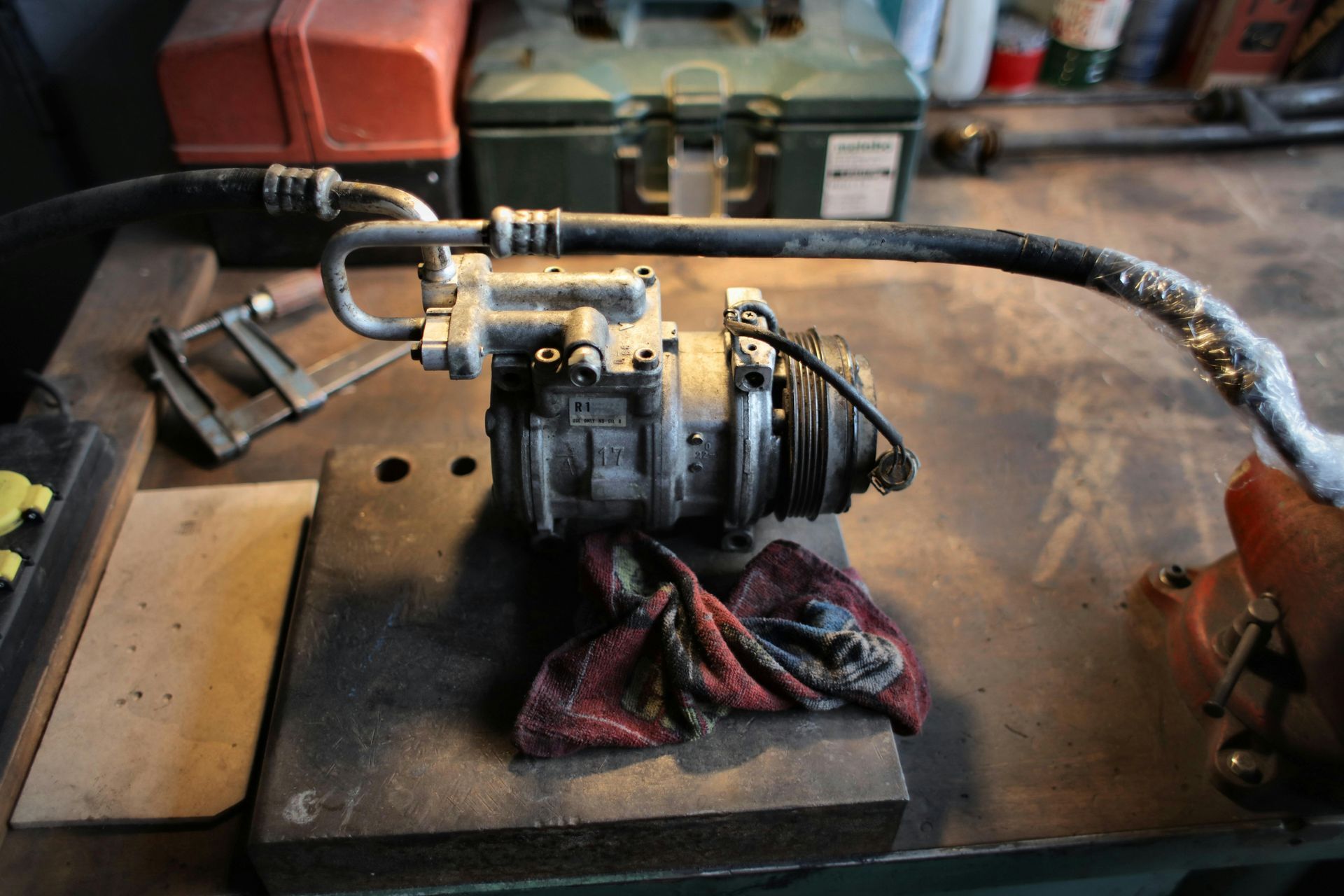 Air conditioning compressor on a workbench with hoses, tools, and a cloth.