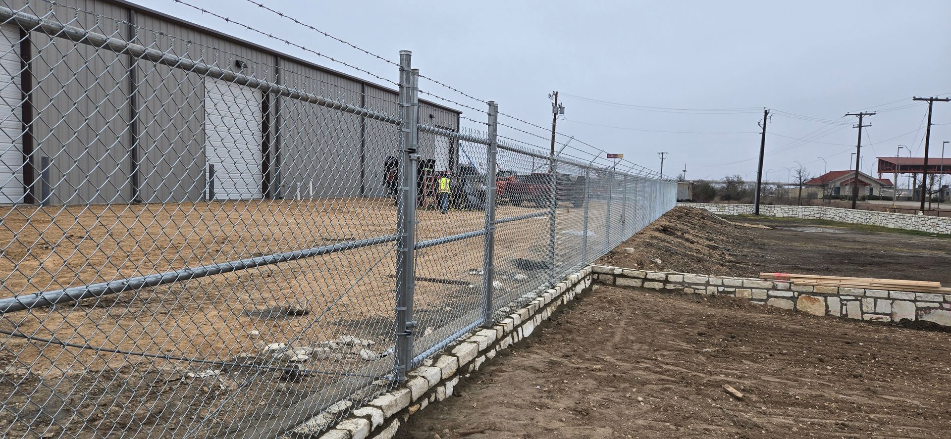 A chain-link fence topped with barbed wire surrounds a construction site.