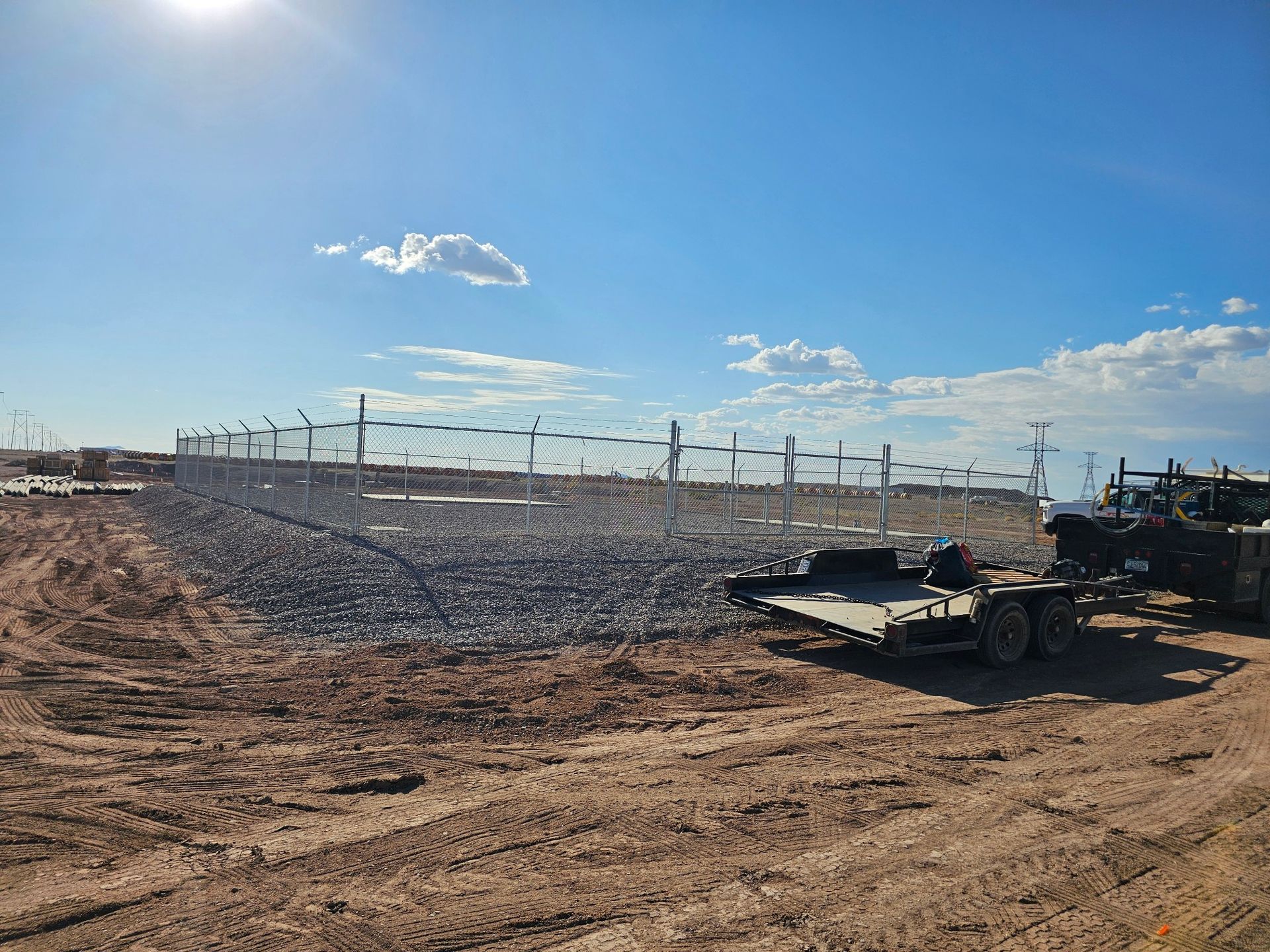An outdoor construction site featuring a circular area enclosed by a tall chain-link fence with a trailer parked nearby