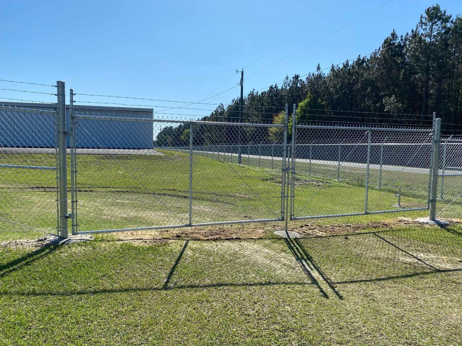 A chain-link fence with two open gates, enclosing a grassy area.
