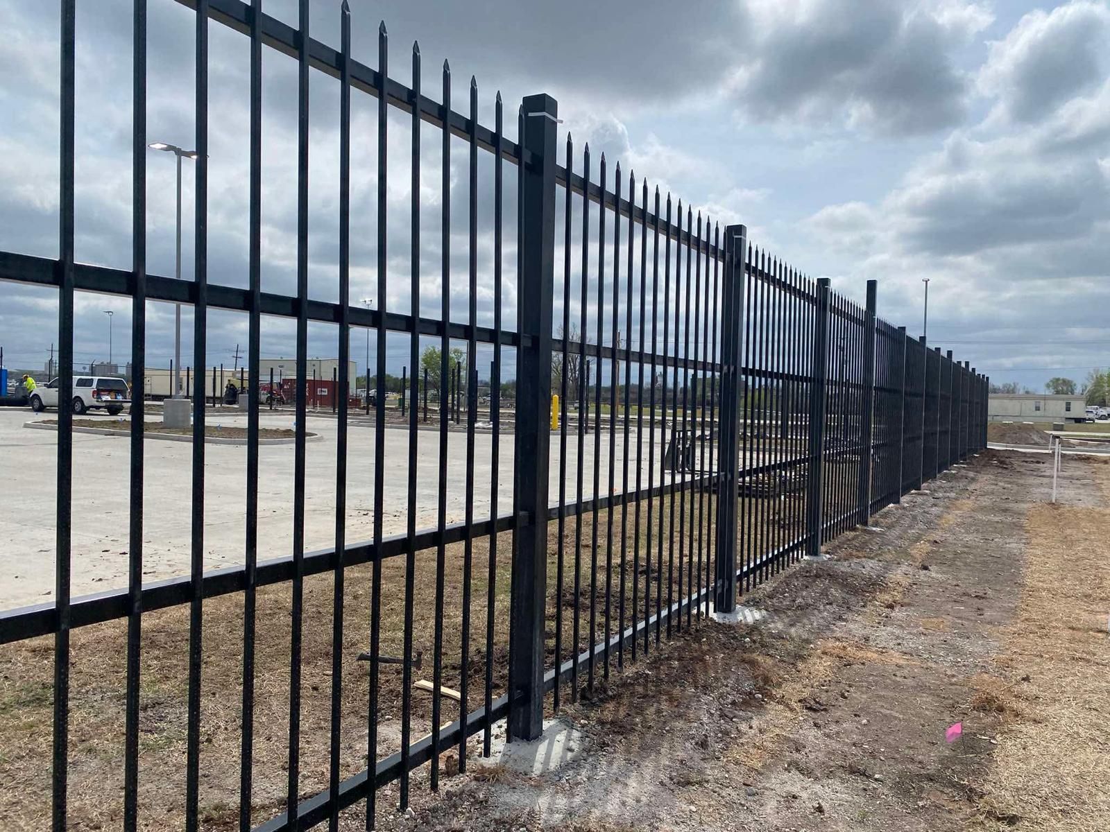 Black metal security fence along a construction site under a cloudy sky.