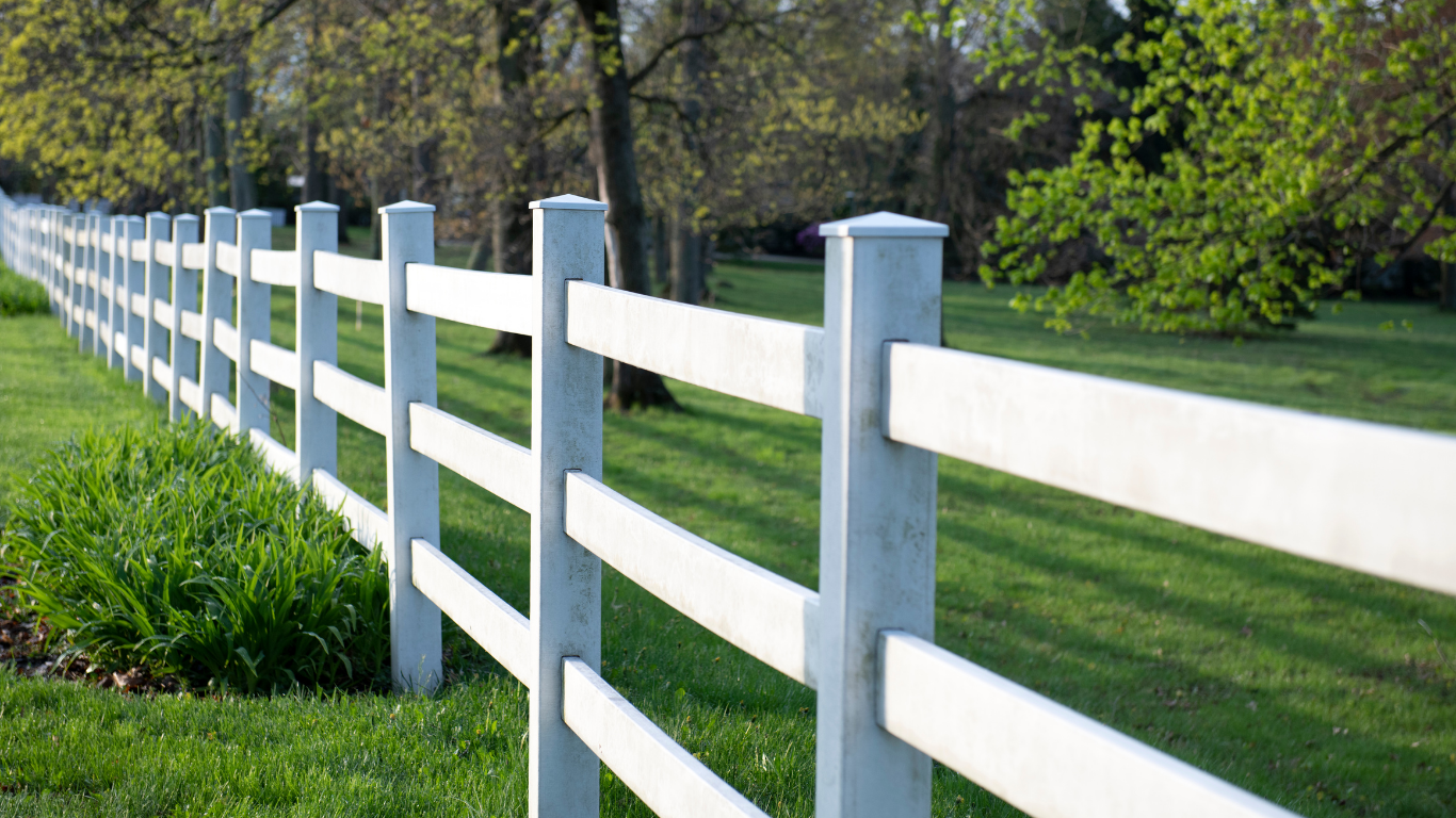 White picket fence in a grassy field with trees in the background.