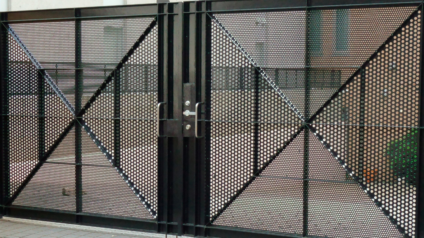 Black metal double gate with diamond mesh design, set against a building facade.
