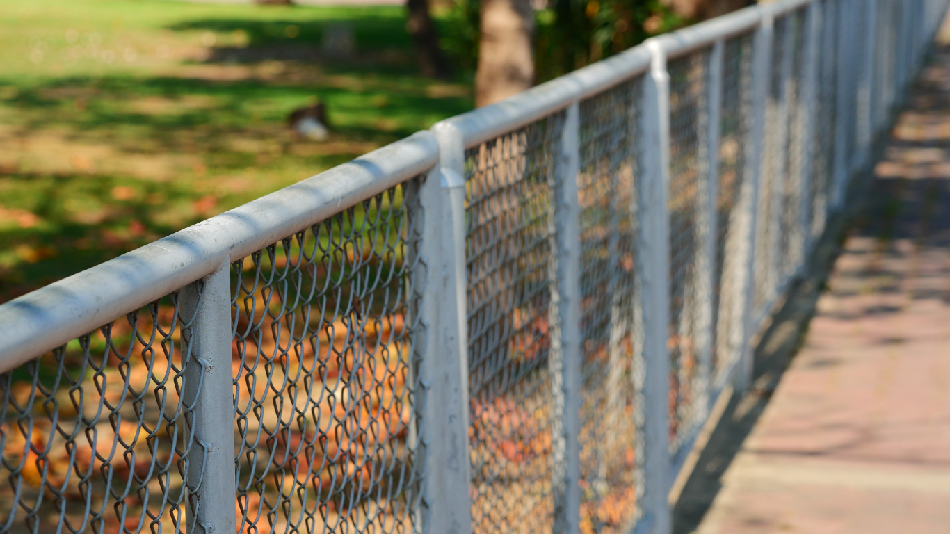 Metal fence with mesh, along a walkway with blurred greenery in the background.