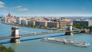 A cruise ship is sailing under a bridge over a river.