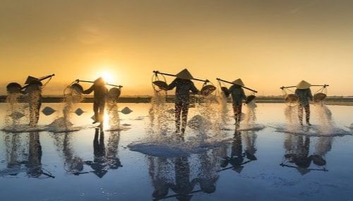 A group of people are walking across a lake at sunset.