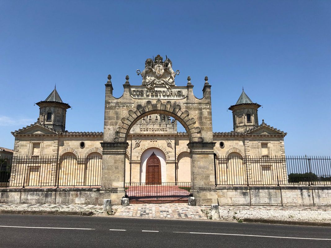 A large stone building with a clock on the top of it is sitting on the side of a road.