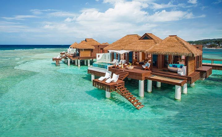 A group of thatched huts on stilts in the middle of the ocean.