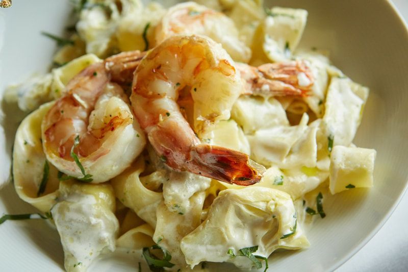 A close up of a plate of pasta with shrimp and artichokes.