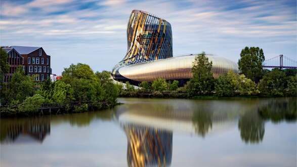 A large building is reflected in a body of water surrounded by trees.