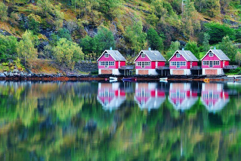 A row of red houses are sitting on the shore of a lake.