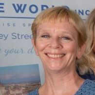 A woman in a blue shirt is smiling in front of a sign.