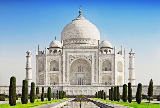 The taj mahal is a very large white building with a blue sky in the background.