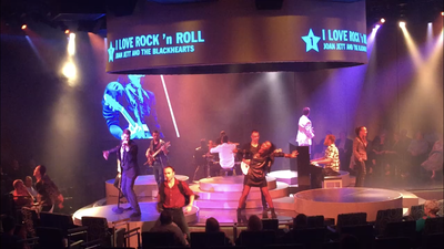 A group of people are standing on a stage in front of a large screen that says i love rock n roll.