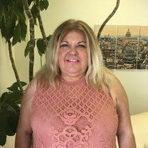 A woman in a pink lace top is standing in front of a picture of a city.