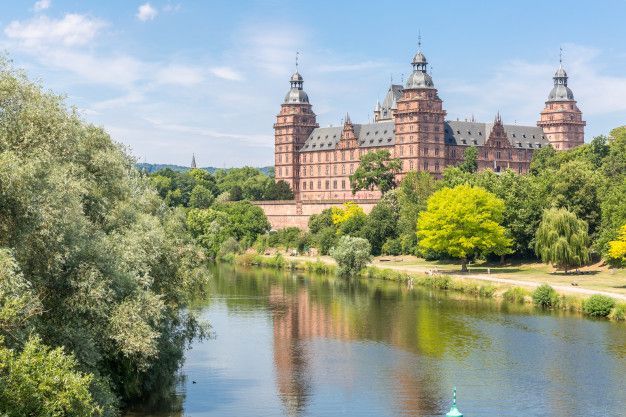 A large castle is sitting on top of a river surrounded by trees.