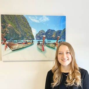 A woman is standing in front of a painting of boats in the ocean.