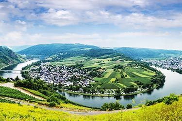 A river flowing through a valley surrounded by mountains and fields.