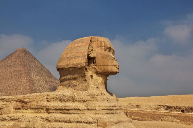 A statue of a sphinx with a pyramid in the background.