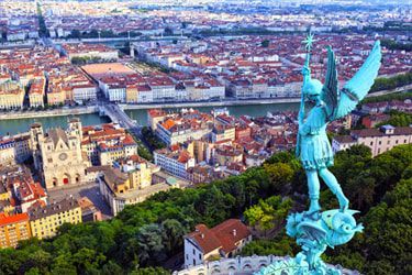 An aerial view of a city with a statue of an angel in the foreground.