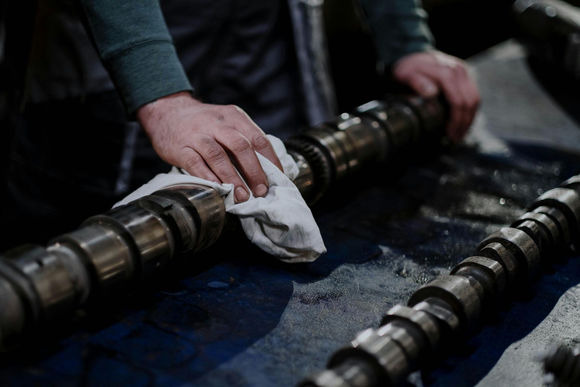 A man is cleaning a camshaft with a towel.