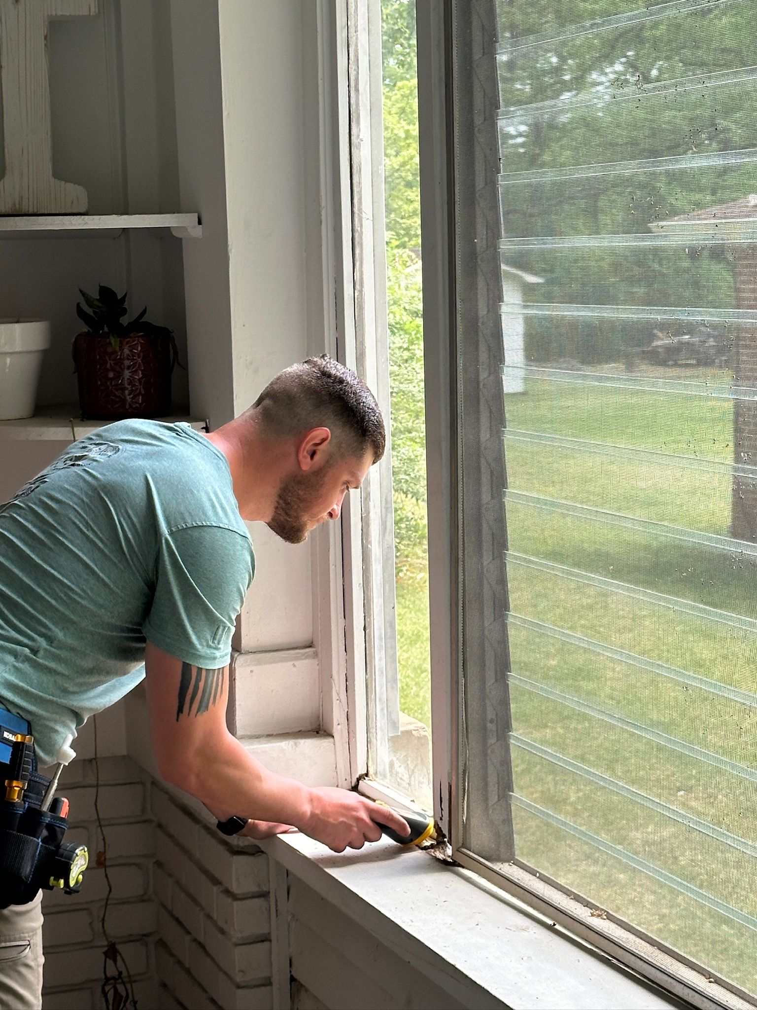 Person repairing a window frame with a tool beside a bright screened window