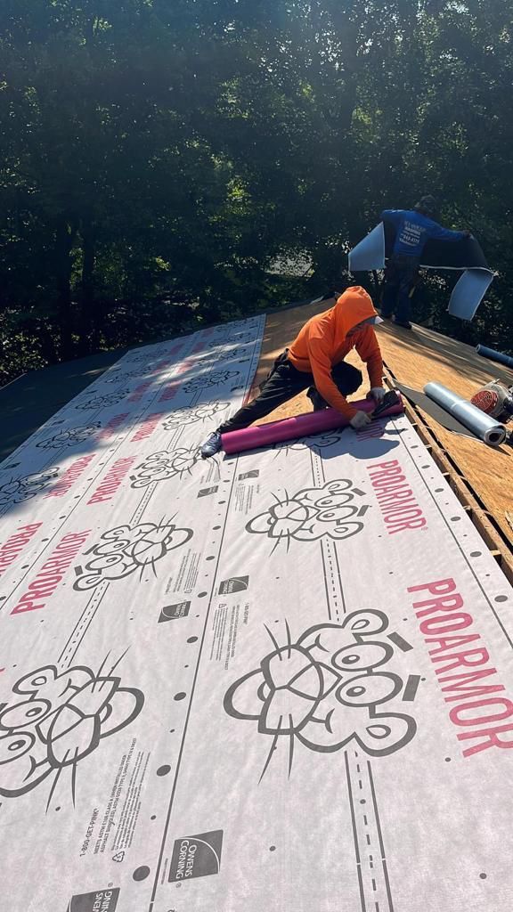 Person stretching on a rooftop, wearing an orange hoodie, next to a pink yoga mat and rolled-up roofing material.