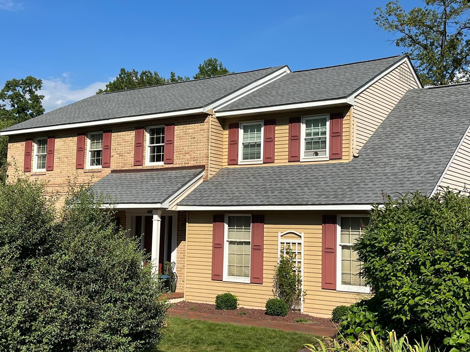 Two-story brick house with a gray roof, maroon shutters, and a blue sky.