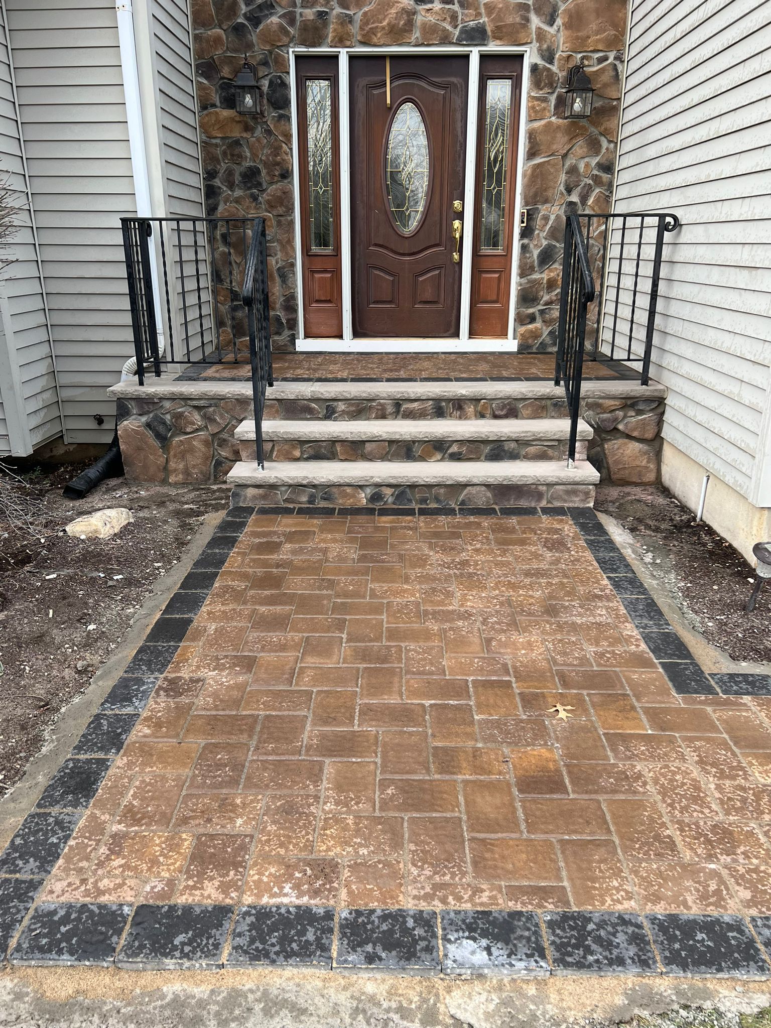 Brick walkway leading to a house with stone steps and a brown door. Black border surrounds the walkway.