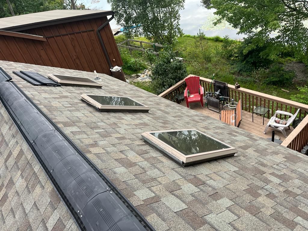 A rooftop with three rectangular skylights, a gutter, and a deck with a red chair in the background.
