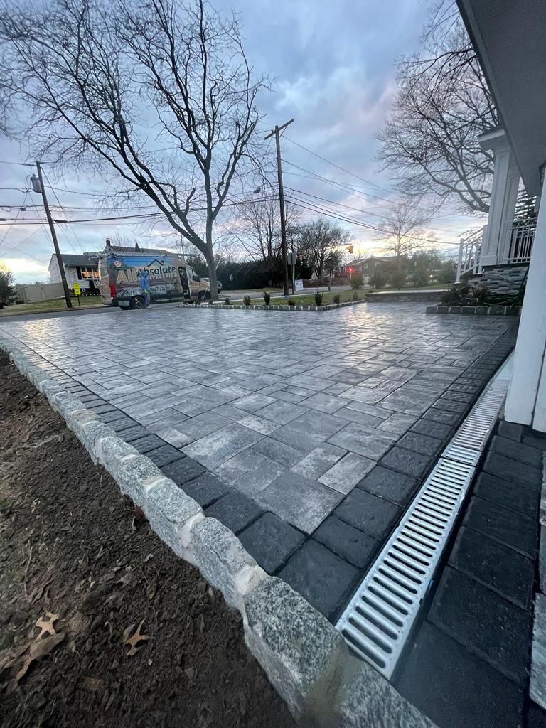 A newly paved driveway with a stone border and a drainage system, set against a cloudy sky.
