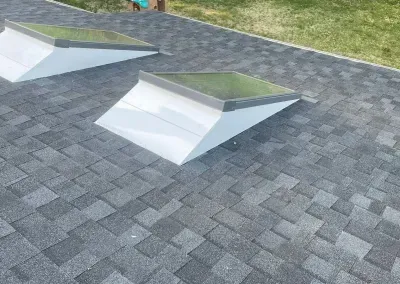 Two skylights on a shingled roof, angled white boxes with grey-green glass tops.