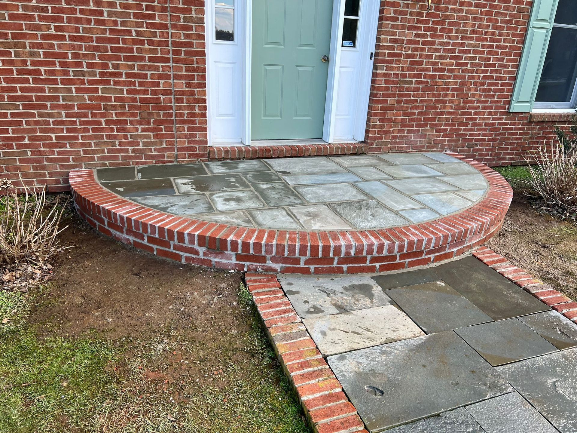 A brick and stone front entrance to a building with a light green door. A semi-circular brick and stone step leads to the doorway.