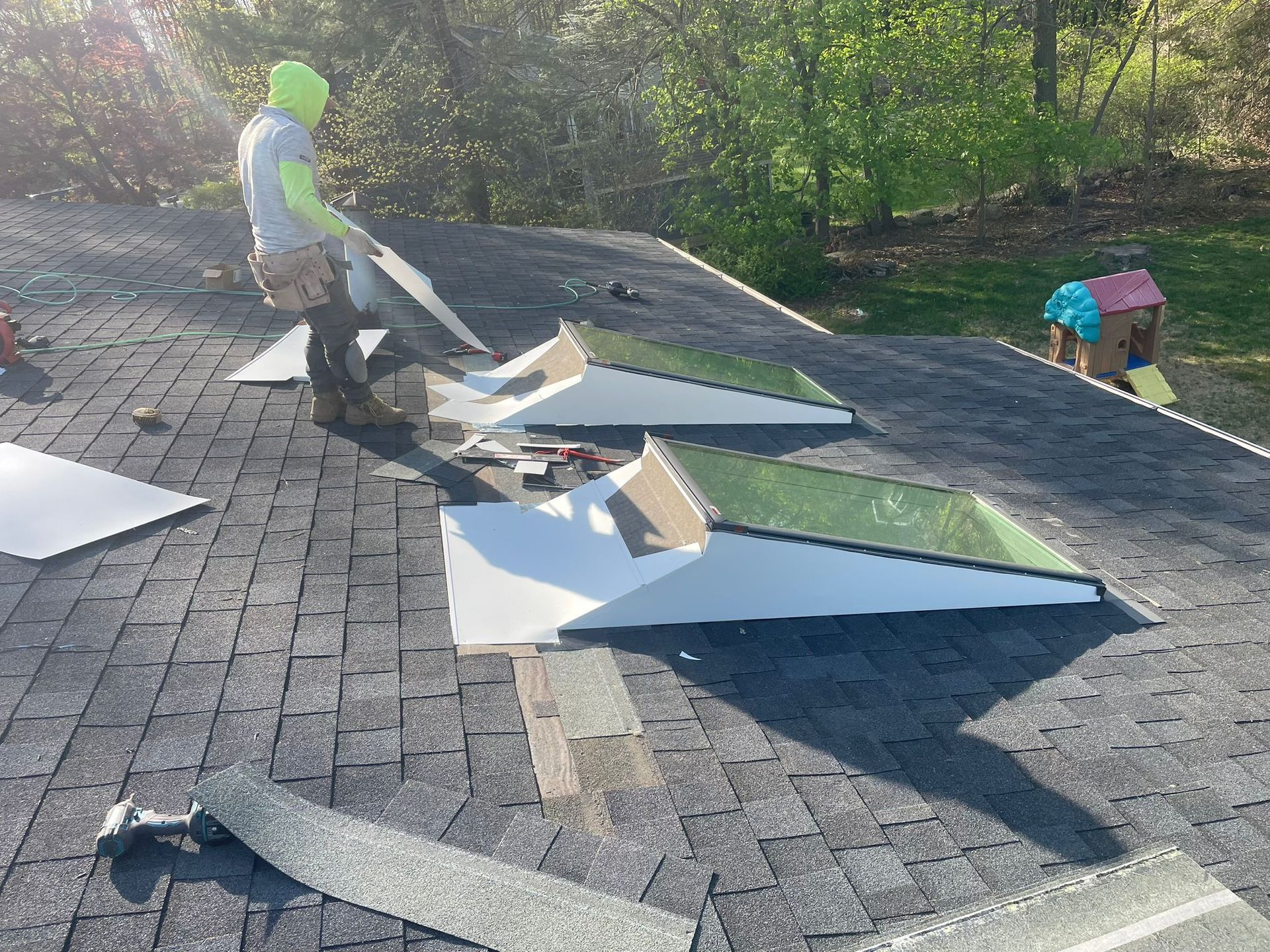 A roofer in neon green headwear works on a roof installing skylights on an overcast day.