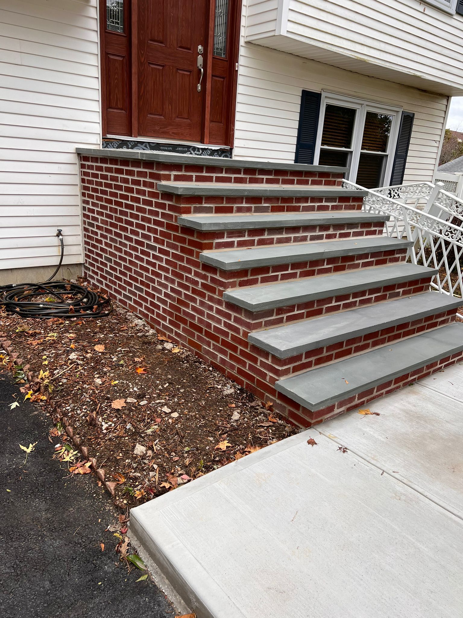 Brick steps leading up to a brown front door. Gray concrete tops the steps and sides. The steps are next to the house and a patch of fallen leaves.