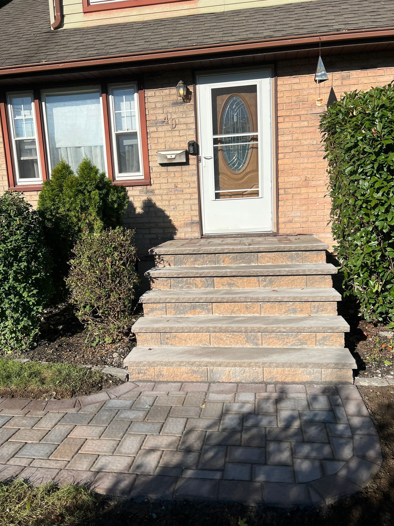 Brick facade house with steps leading to a front door. Landscaping includes bushes and a brick walkway.