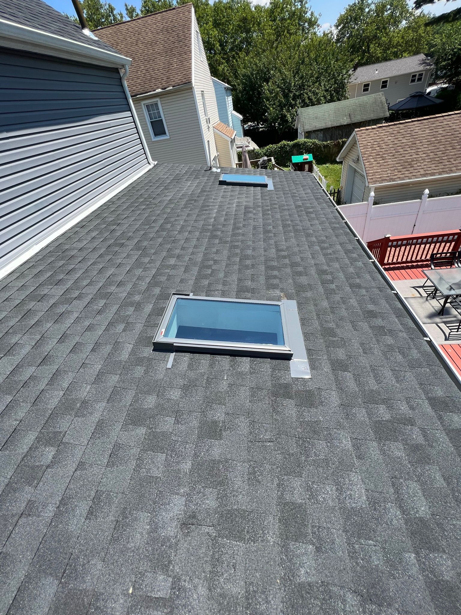 View from above of a dark gray shingle roof with two skylights and a section of a blue house.
