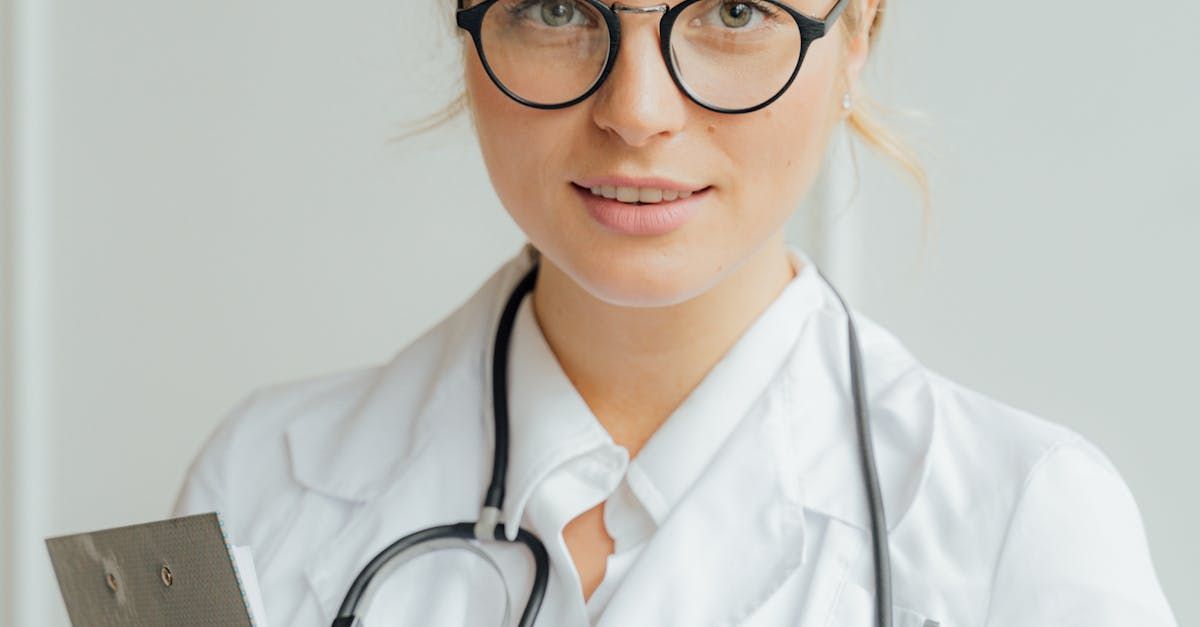 A female doctor wearing glasses and a stethoscope is holding a cell phone.