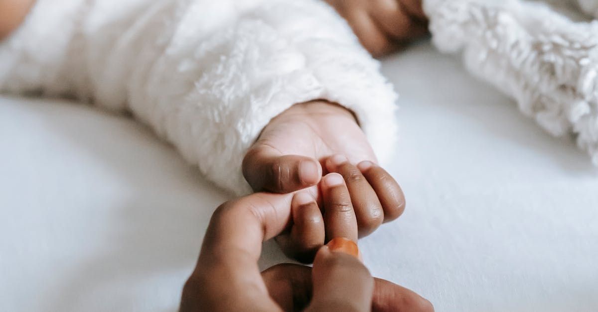 A person is holding a baby 's hand on a bed.