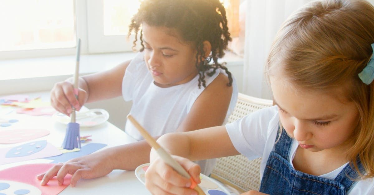 Two little girls are sitting at a table painting with brushes.