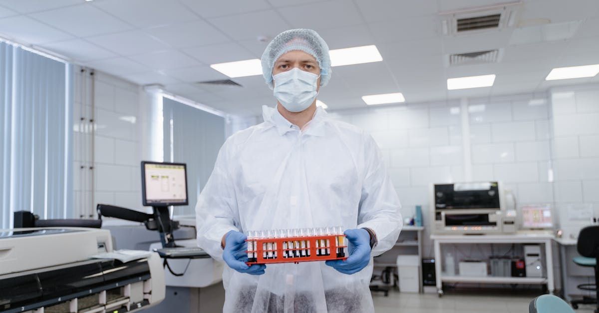 A man in a lab coat and mask is holding a box of test tubes.