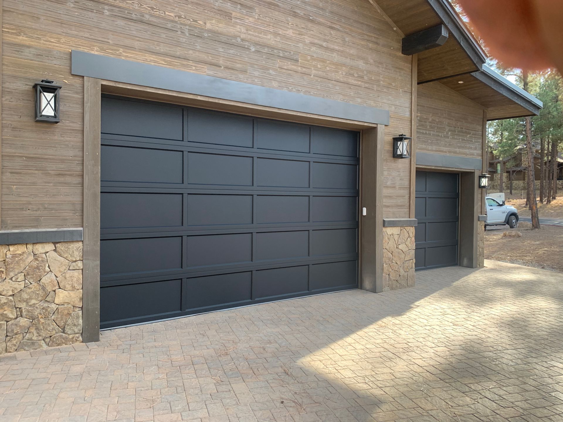 A modern home exterior with two black garage doors, stone and wood siding, and a paved driveway.