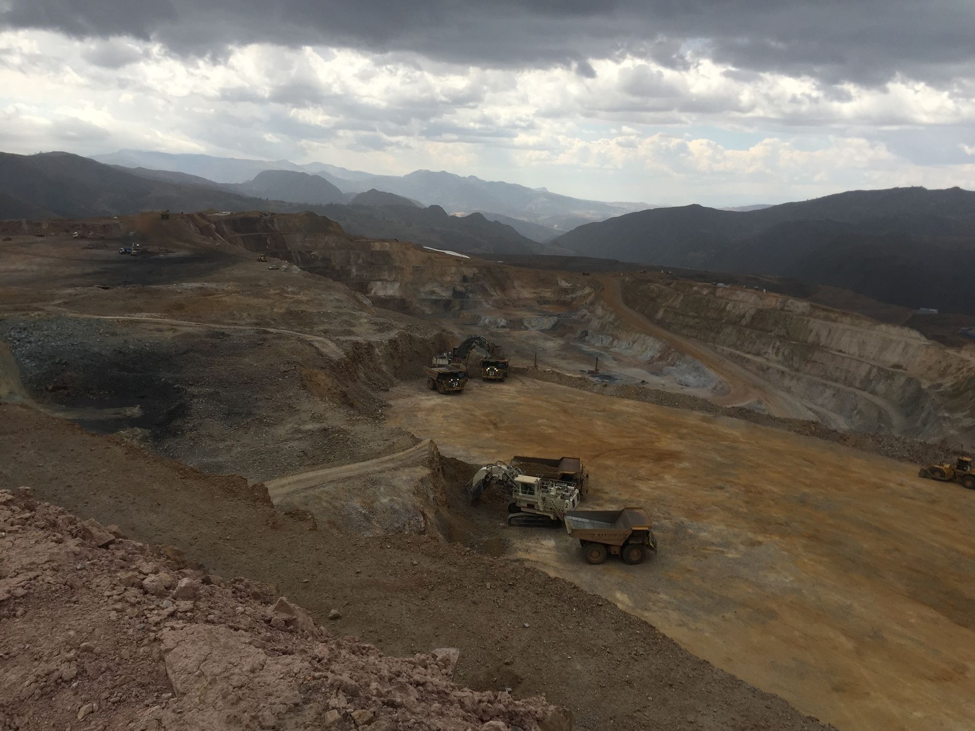 Four people in a modern office, gathered around a table; man with glasses gestures while speaking, laptop visible.