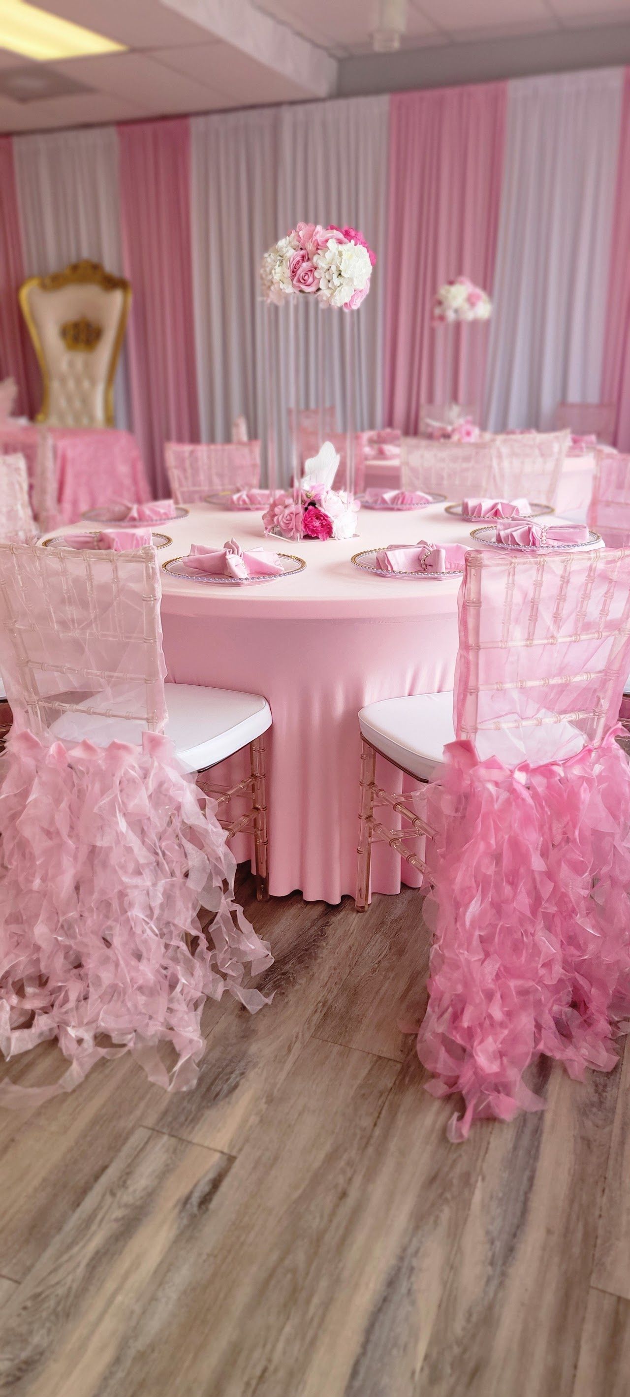 A pink-themed party with round tables, chairs, and decorations. Drapes and flowers add to the ambiance.