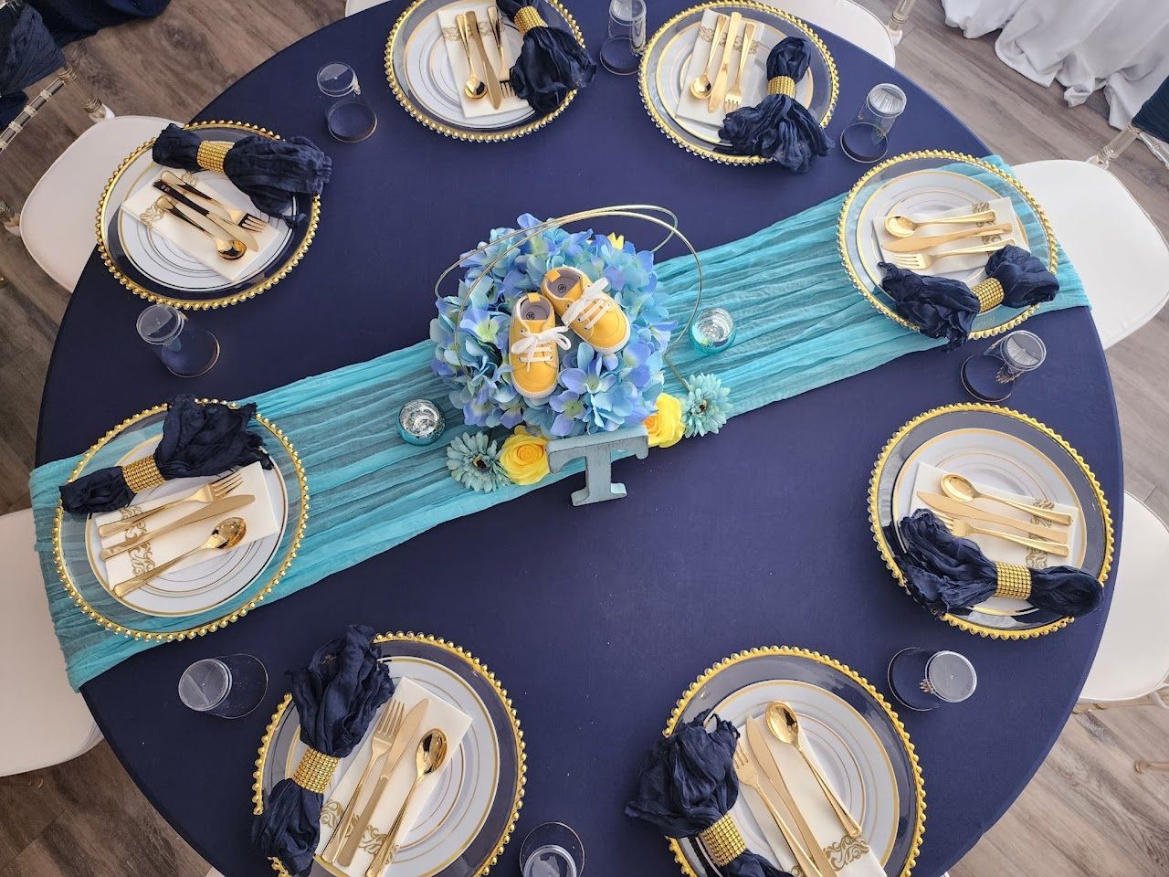 Navy blue table set for a baby shower with gold accents, center floral arrangement, and blue runner.