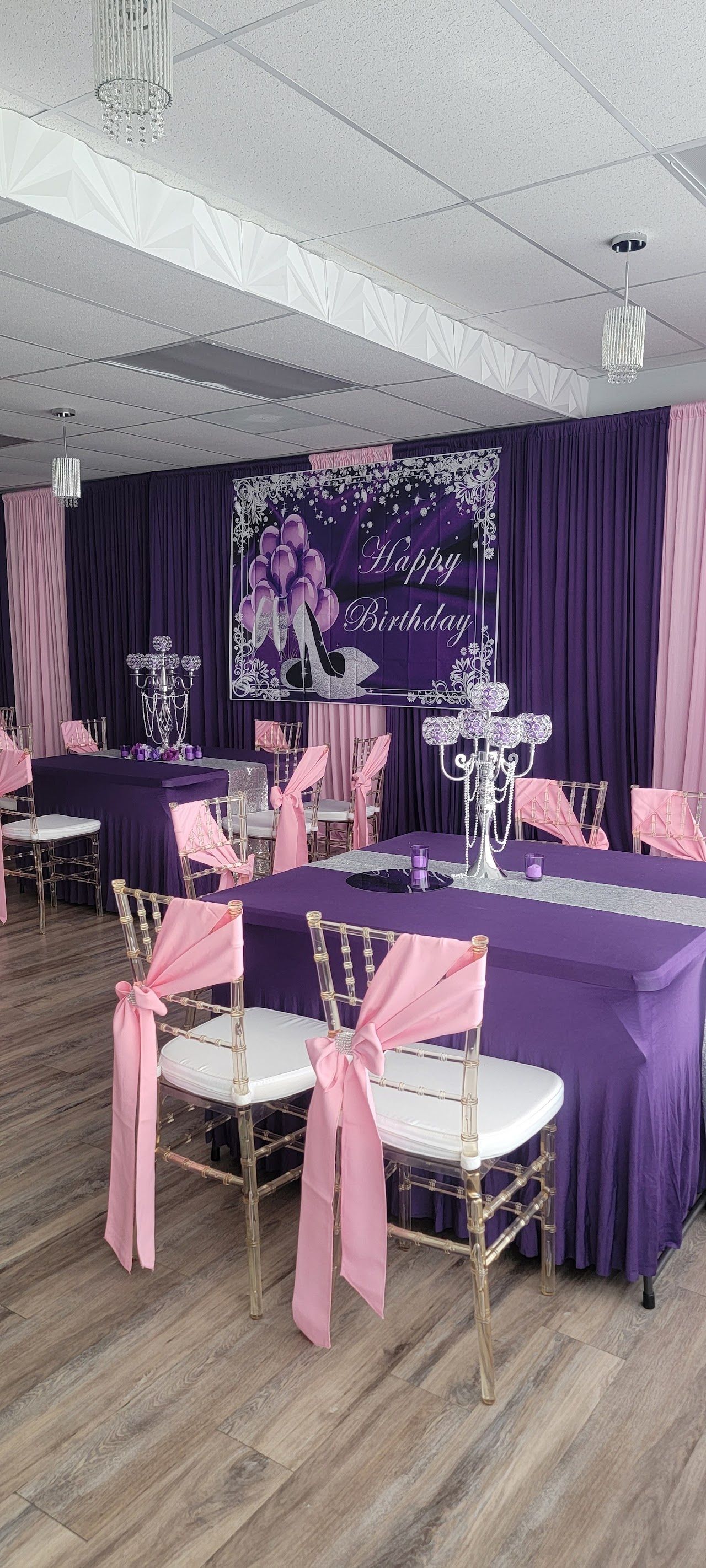 A decorated room with purple and pink accents, tables, and chairs, ready for an event.